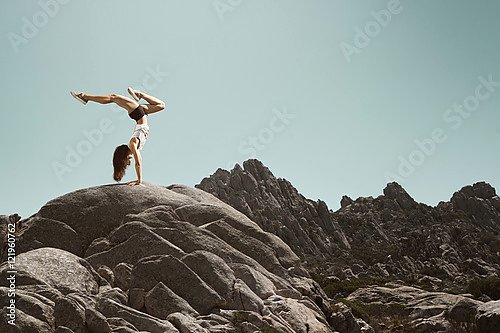 Женщина делает стойку на руках на скале