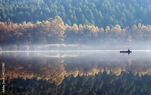 Лодка на туманном озере на фоне осеннего леса