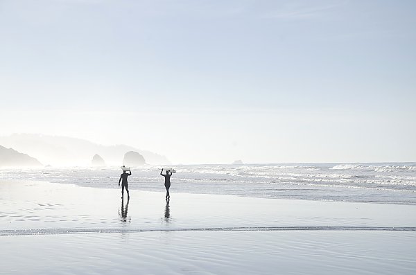 Силуэты двух человек, несущих доски для серфинга над головами на мокром пляже