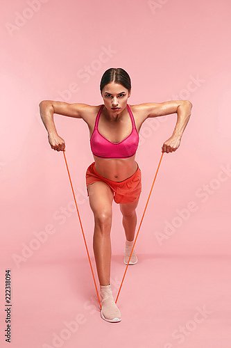 Спортсменка с эспандером на розовом фоне
