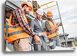 Постер bottom view of builders and architect discussing blueprint at construction site