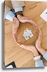 Постер Couple making circle with hands on wooden table with paper house inside, house insurance