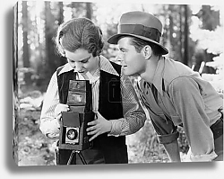 Постер Smiling boyfriend looking at girlfriend using video camera in forest