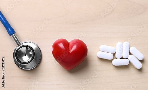 Красное сердце с стетоскопом и таблетками на столе