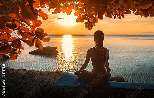 Медитирующая девушка у моря на закате
