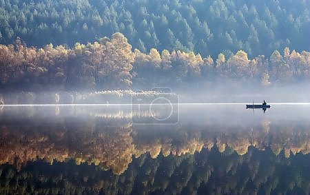 Лодка на туманном озере на фоне осеннего леса