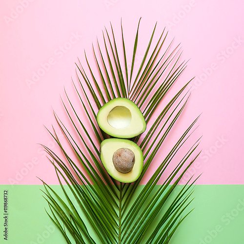 Спелый авокадо на пальмовом листе на цветном фоне