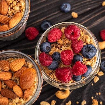 closeup of delicious granola with berries, dried apricots, nuts and yogurt in glass cups on wooden surface